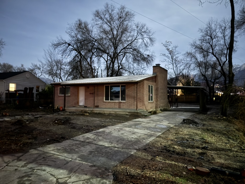 The brick house with its front porch, chimney and carport